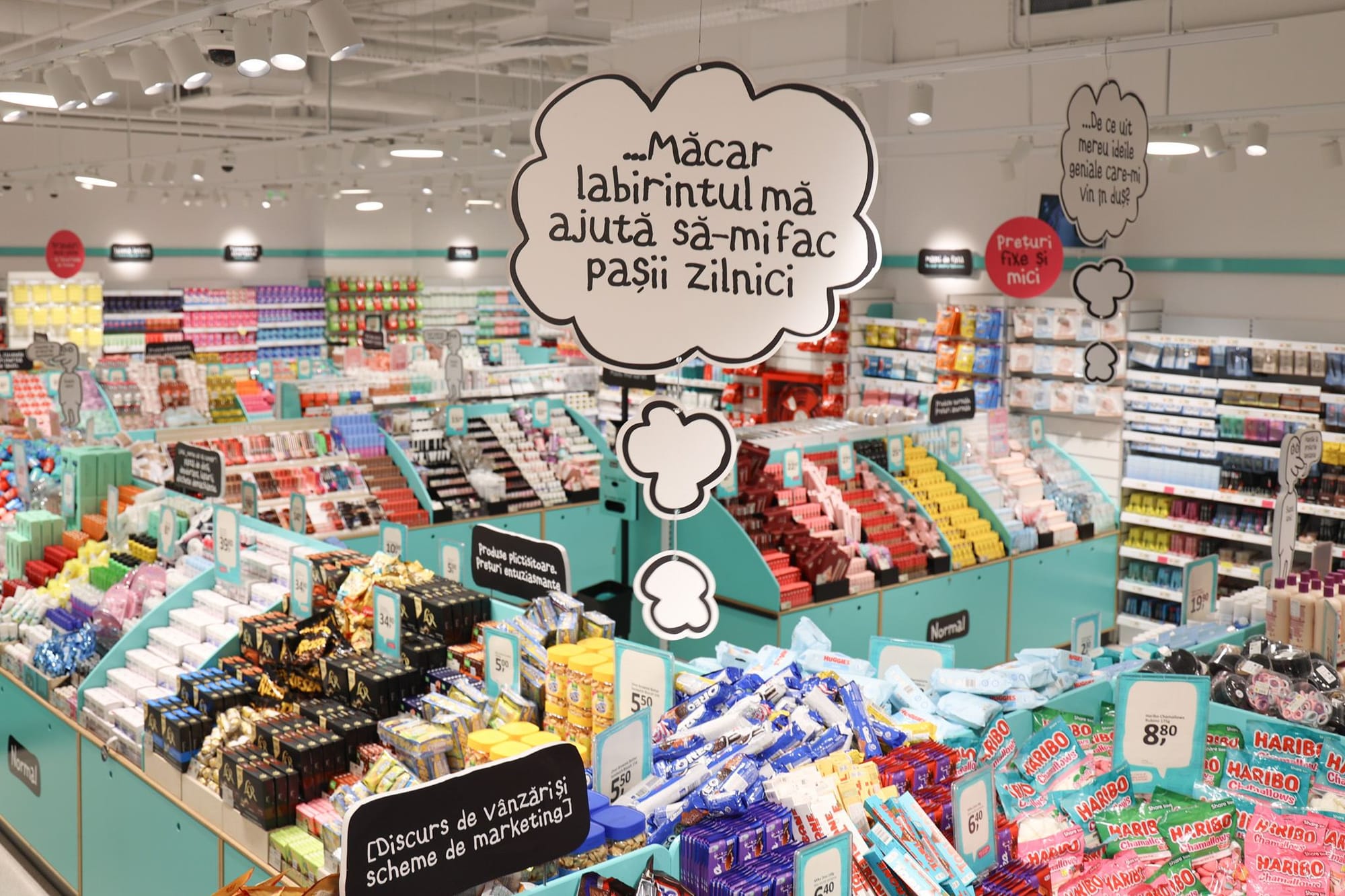 Interiorul unui magazin NORMAL, cu rafturi turcoaz de cosmetice și dulciuri și un balon de benzi desenate pe care scrie „Măcar labirintul mă ajută să-mi fac pașii zilnici”