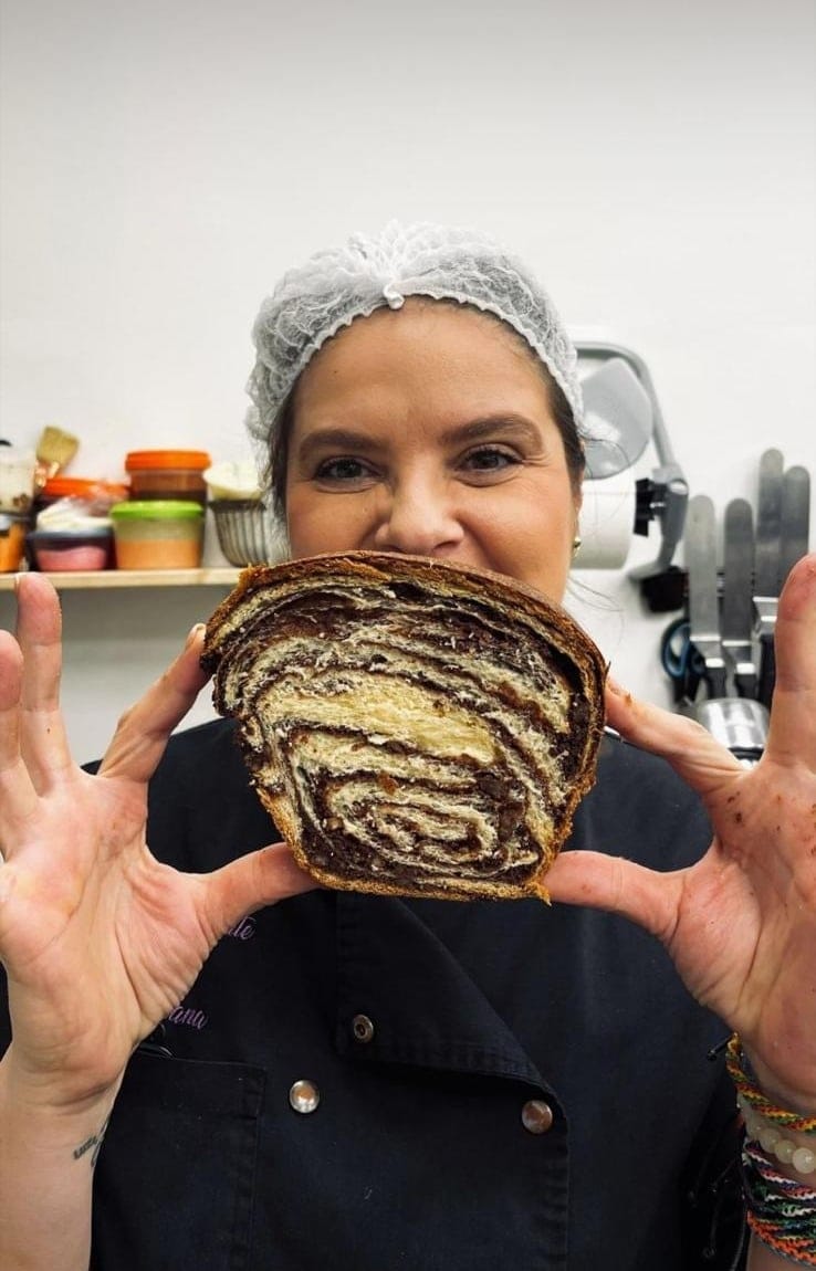 Cofetăreasă cu bonetă care ține în mâini o felie mare de cozonac cu nucă și cacao
