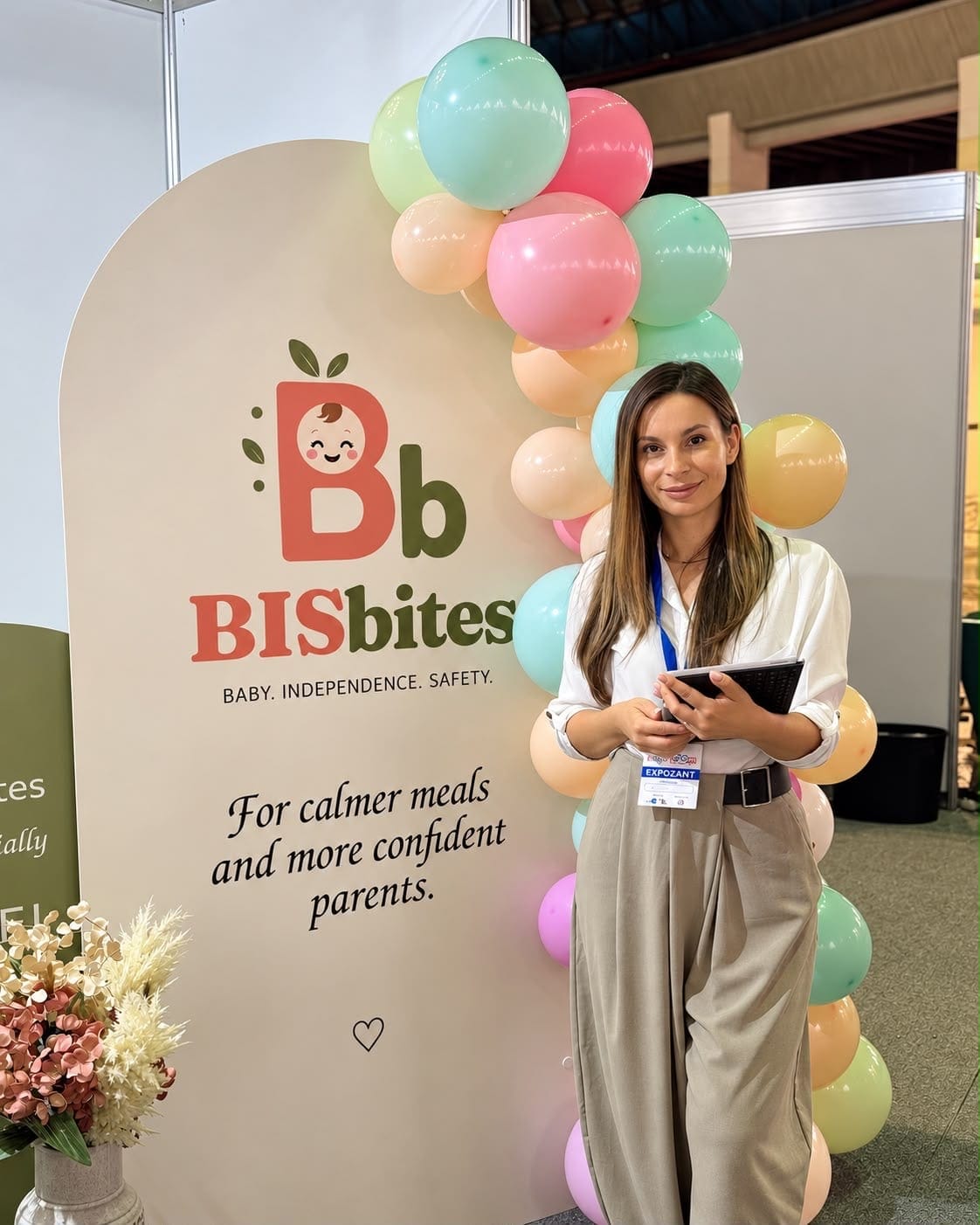 Tânără cu ecuson de expozant lângă un panou BISbites cu baloane colorate