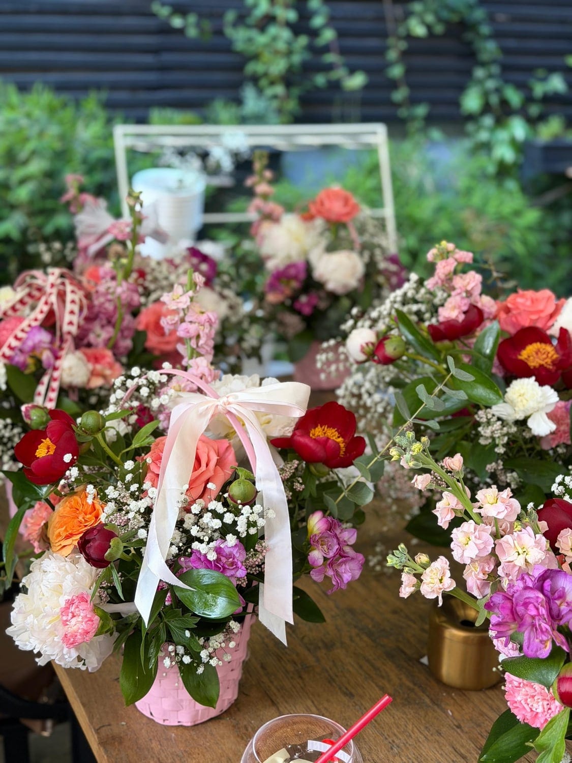 Aranjamente florale cu bujori, trandafiri și gypsophila, legate cu panglici, pe o masă de atelier