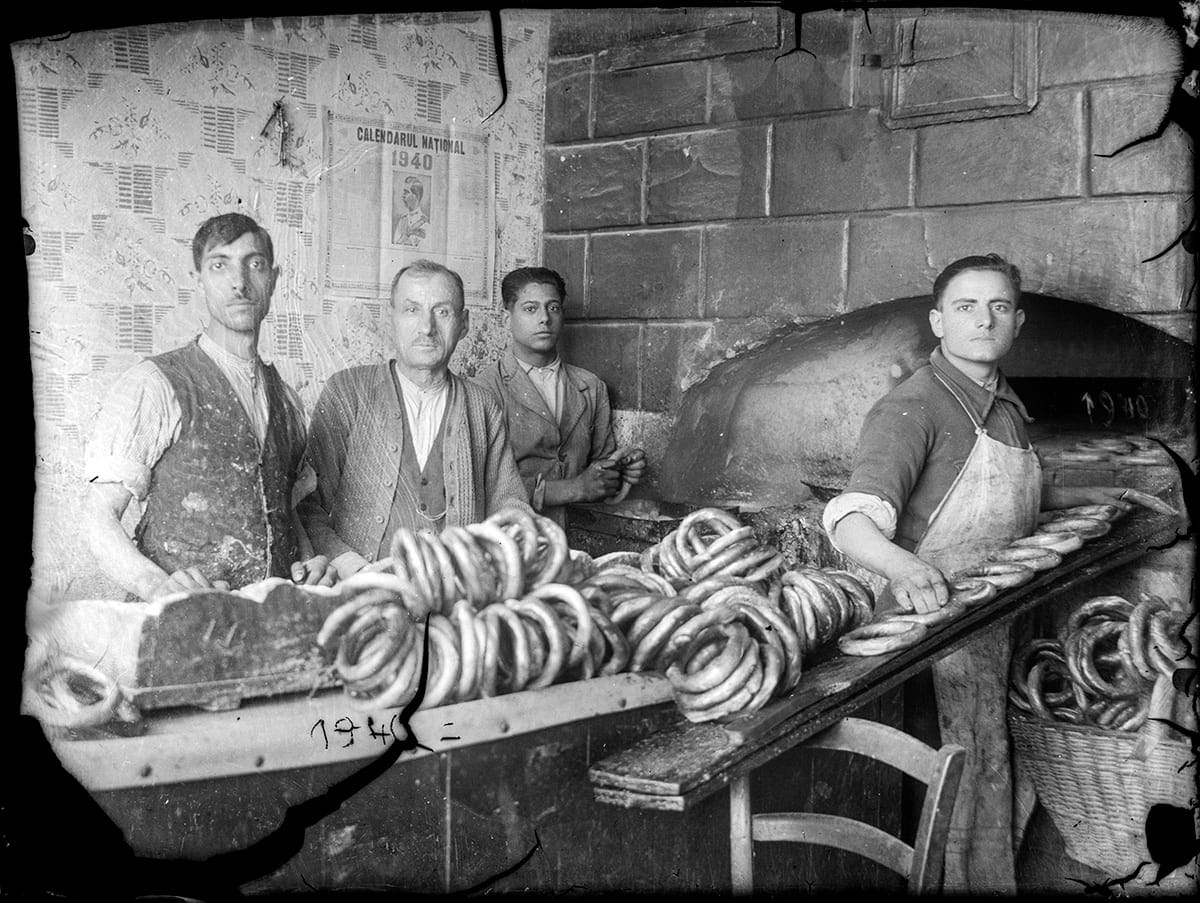 Patru brutari în fața cuptorului, cu mese pline de covrigi, într-o fotografie din 1940