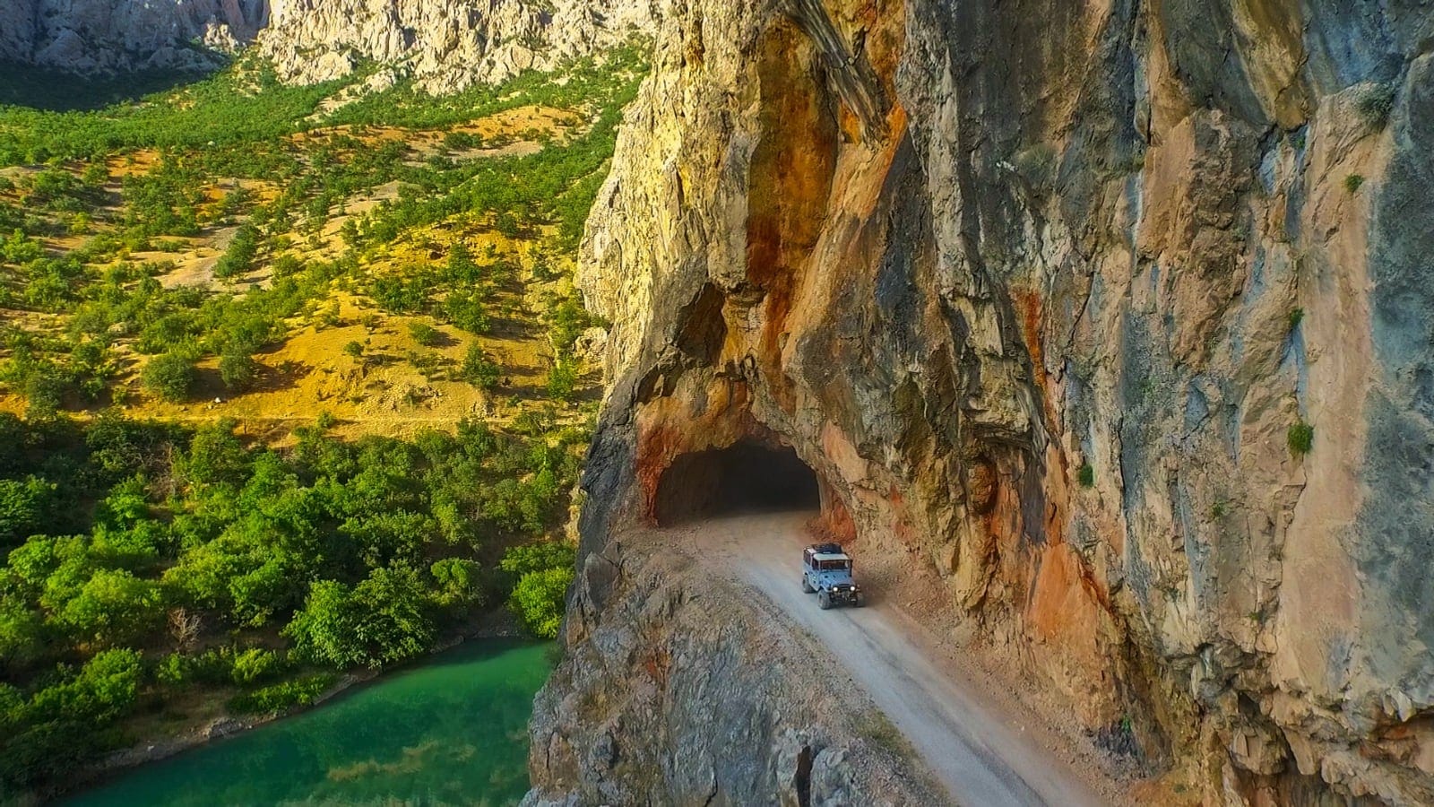 Un vehicul de teren iese dintr-un tunel săpat în stâncă, deasupra unei văi verzi cu un râu