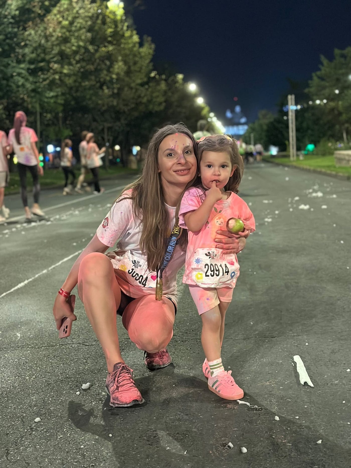 Mamă și fetiță acoperite de pudră colorată, cu numere de concurs, la The Color Run