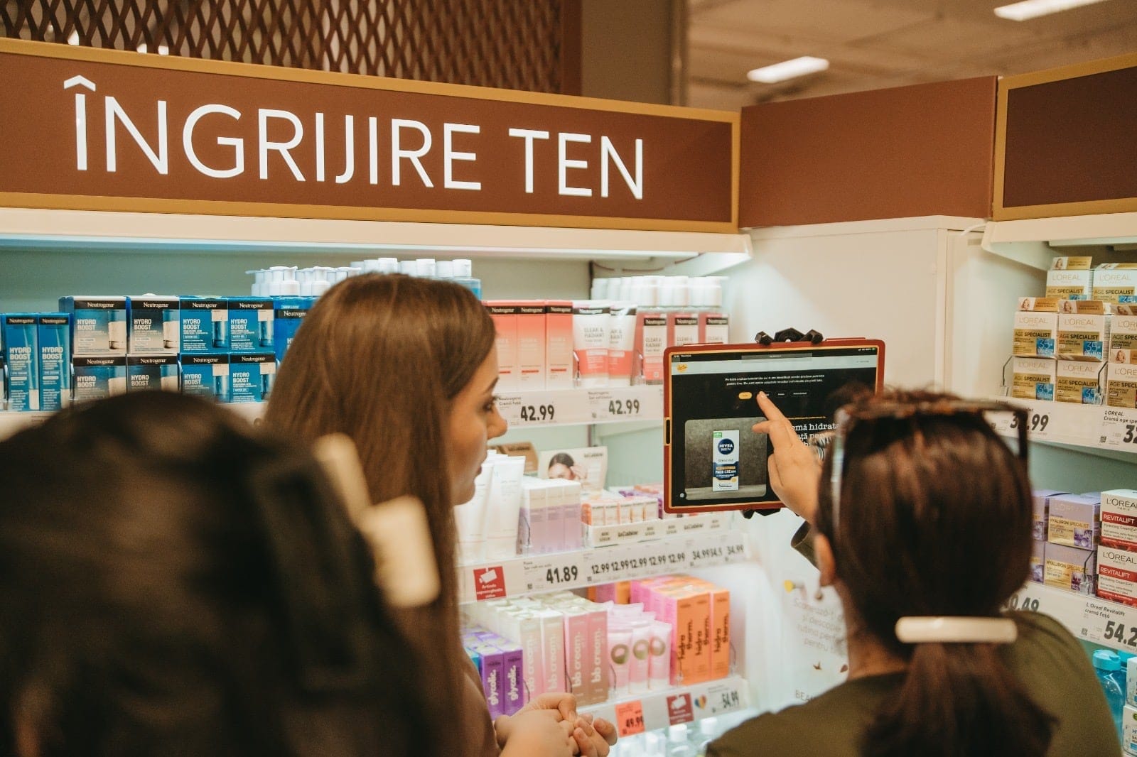 Două cliente în fața raftului Îngrijire ten, la o tabletă care recomandă produse