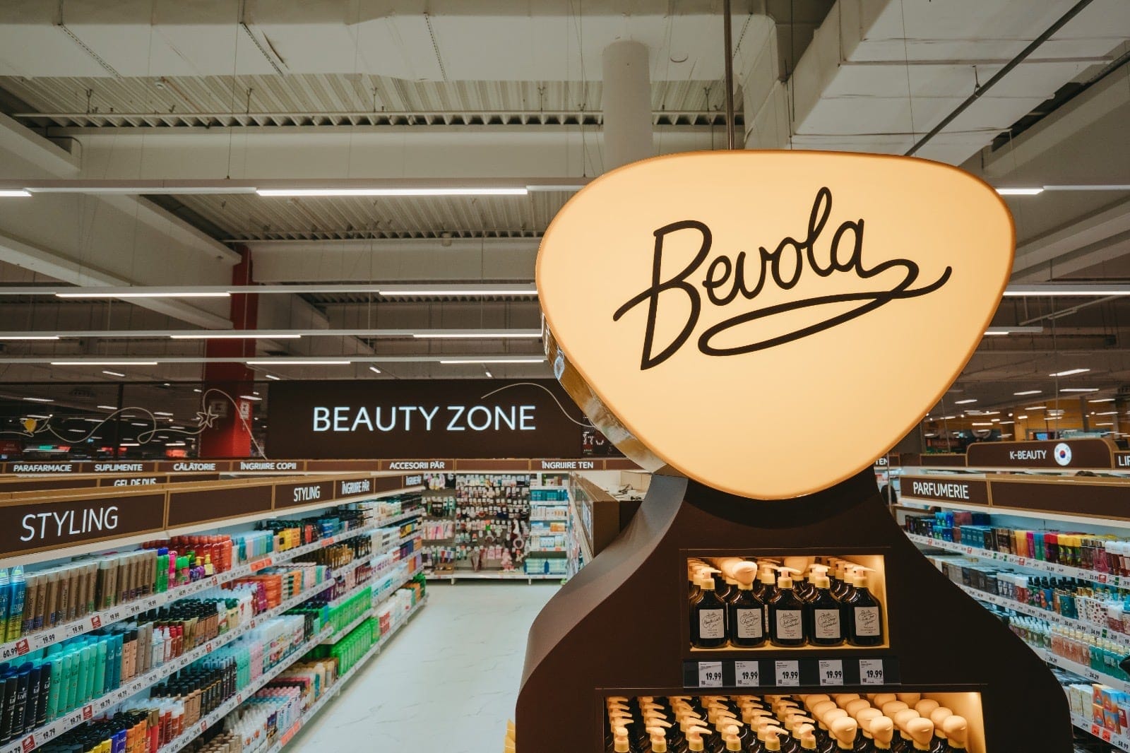 Stand luminat cu produsele Bevola, în fața rafturilor din zona Beauty Zone