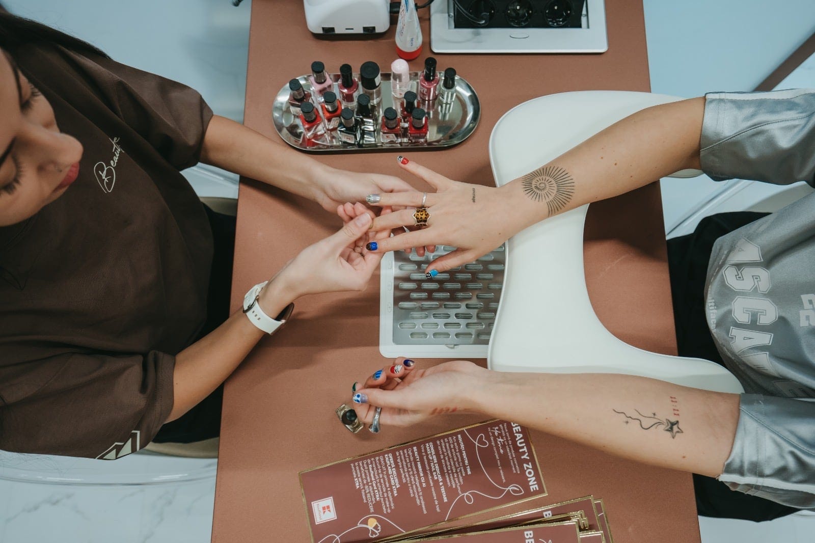 Manichiuristă care aplică ojă unei cliente, la masa din Nail Bar