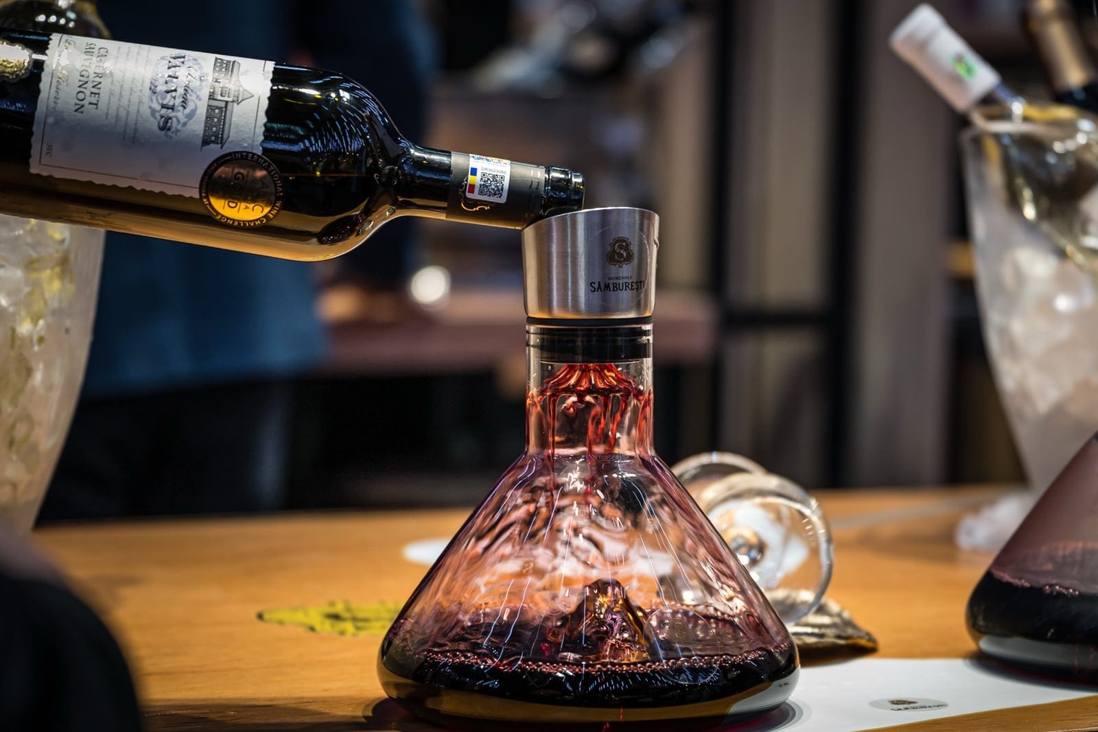 Vin roșu turnat dintr-o sticlă într-un decantor de sticlă, pe o masă de degustare
