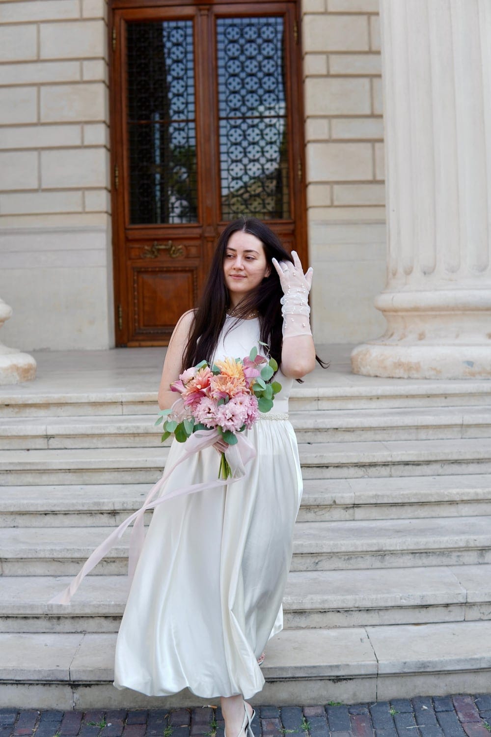 Femeie în rochie albă, cu un buchet de flori, pe treptele unei clădiri vechi