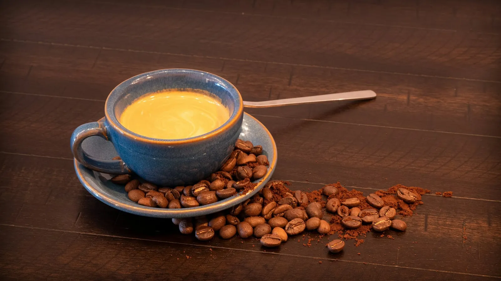O ceașcă de cafea pe o farfurioară, cu boabe de cafea în jur