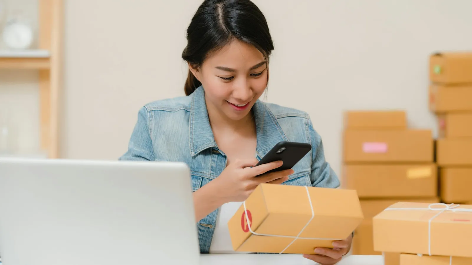 O tânără fotografiază cu telefonul un colet primit, lângă un laptop și alte cutii
