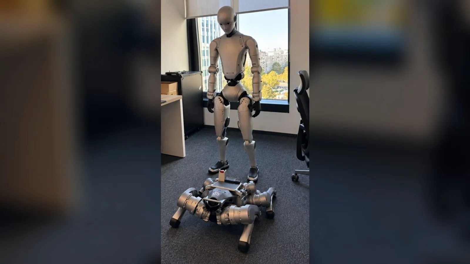 Un robot umanoid argintiu stă în picioare într-un birou, lângă un robot patruped cu patru picioare