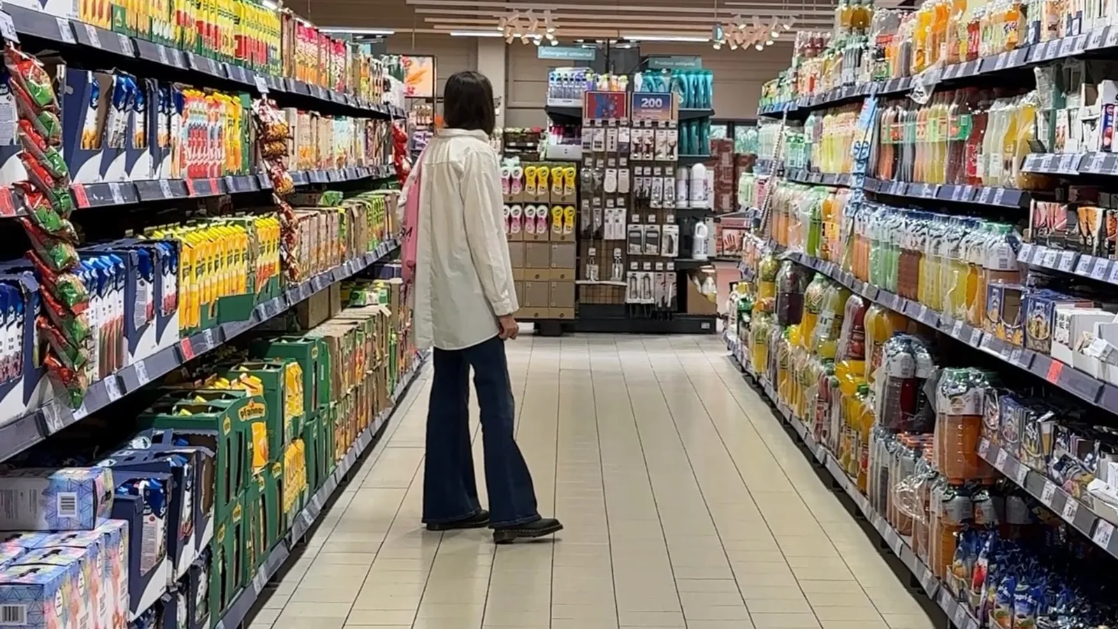 Clientă pe un culoar de supermarket, între rafturi cu sucuri
