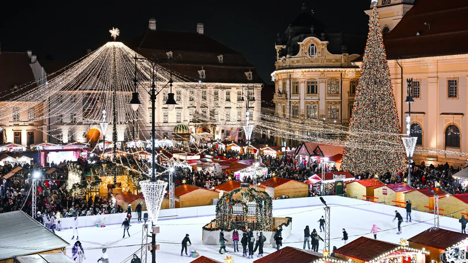 Târgul de Crăciun din Piața Mare din Sibiu, noaptea, cu brad luminat, patinoar și căsuțe de lemn